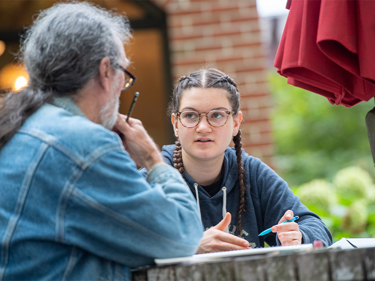 A student speaks with an instructor at an outdoor table.